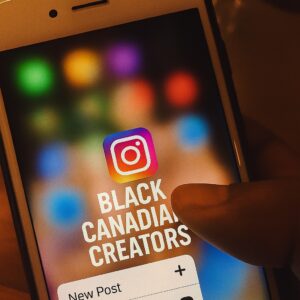 A close-up of a smartphone screen showing the Instagram app icon, with a person's thumb hovering over the “New Post” option. The screen background is softly blurred with colorful app icons, and the words "Black Canadian Creators" are prominently added to the Instagram logo area.